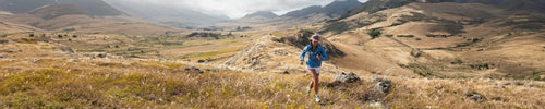 Person hiking through a scenic landscape with mountains and open fields.